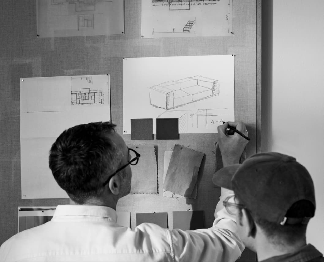 Two designers pinning furniture sketches and fabric swatches to a studio wall
