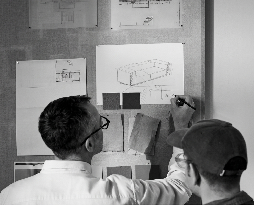 Two designers pinning furniture sketches and fabric swatches to a studio wall